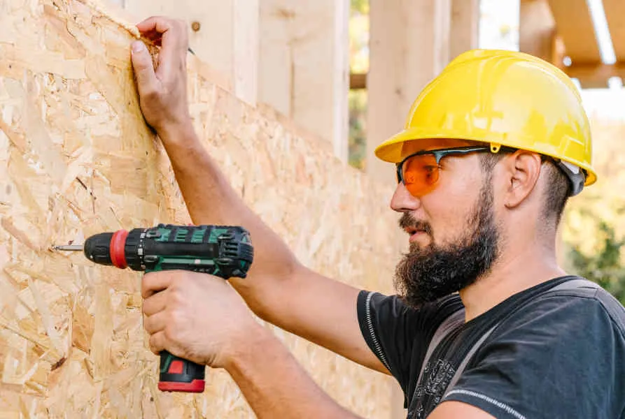 Řemeslník kotví OSB desku na dřevěnou konstrukci stěny